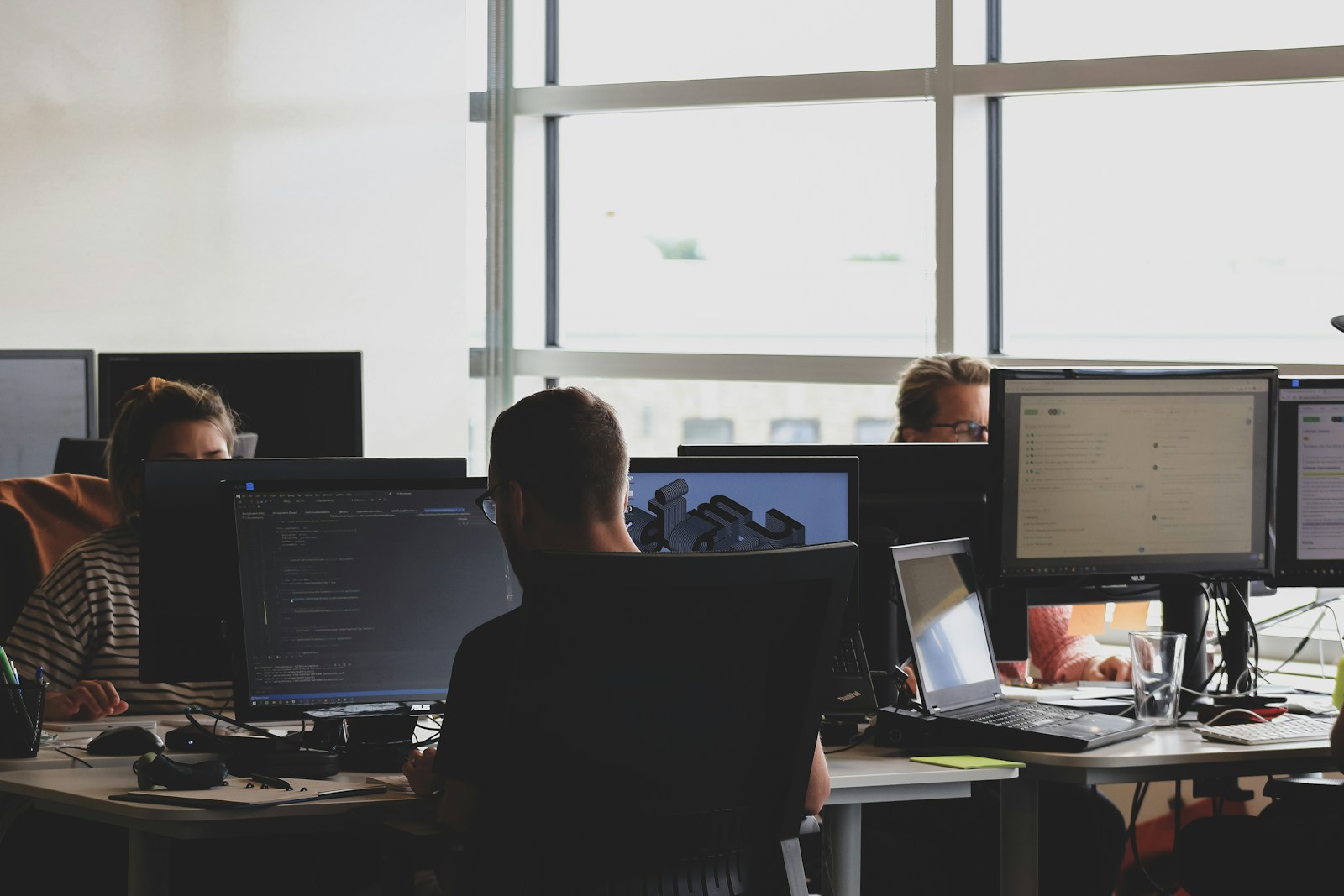 Team working at desks with multiple monitors in a backlit office